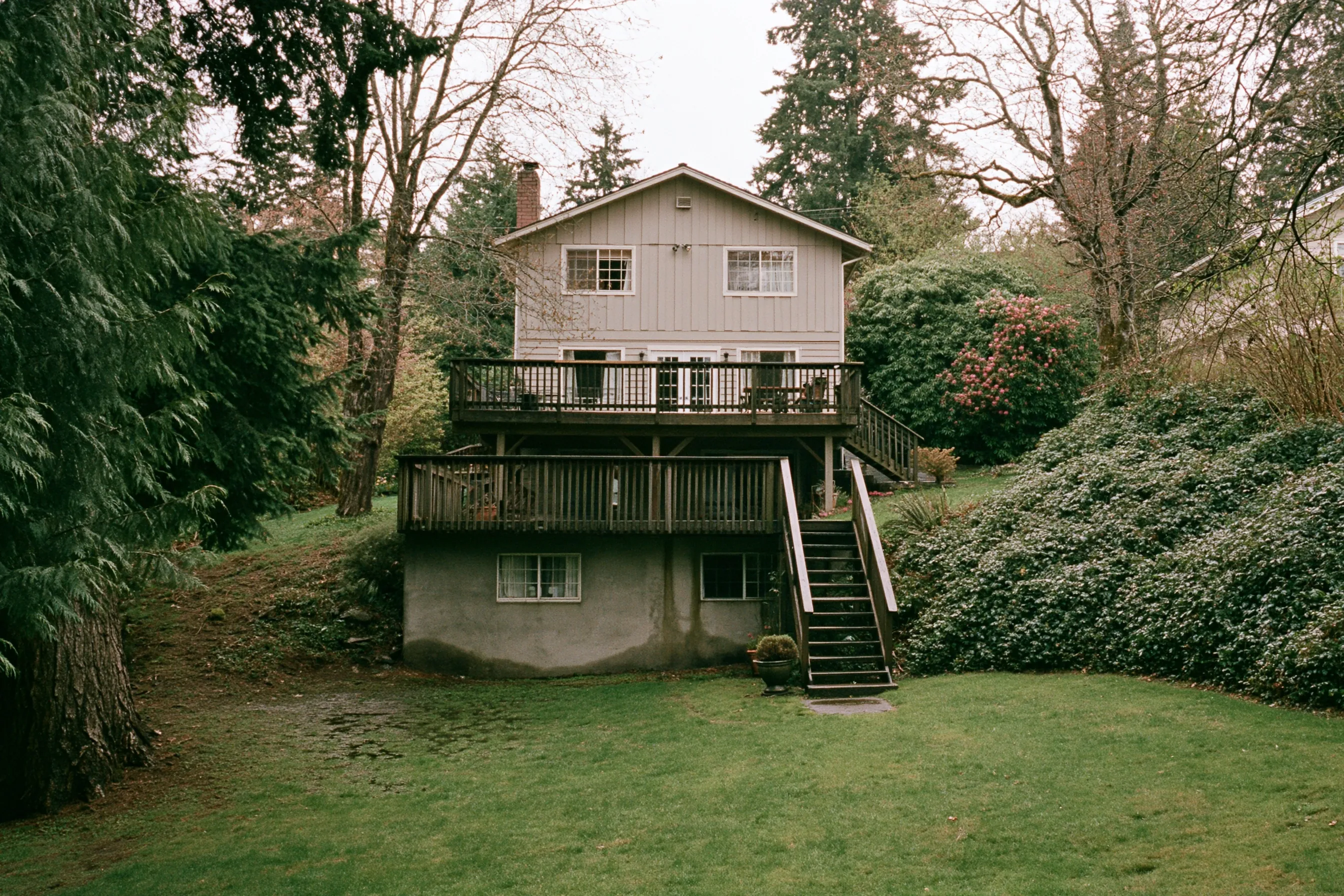 Rear of a two-story house on a gentle slope with a daylight basement, a poured concrete wall at the lower level and a deck above
